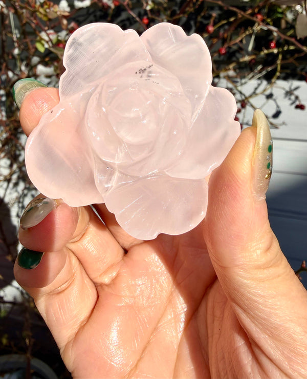 A hand holding a rose carved out of mangano calcite