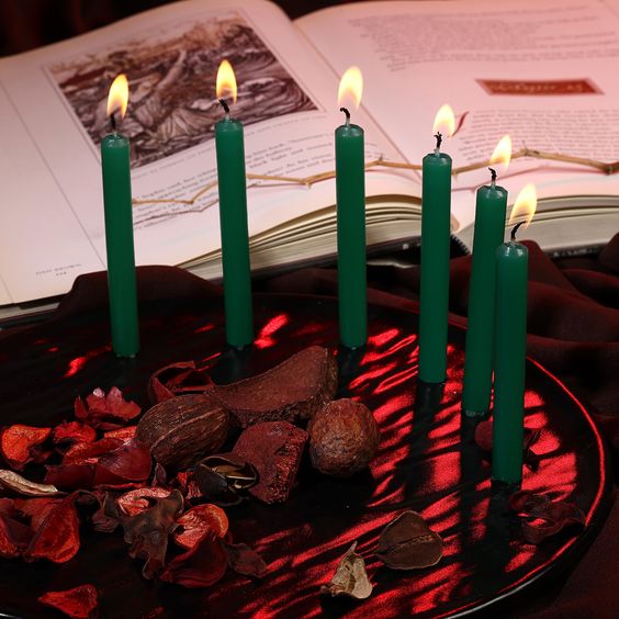 Green candles on a red plate surrounded by spell accoutrements and an open book can be seen in the background