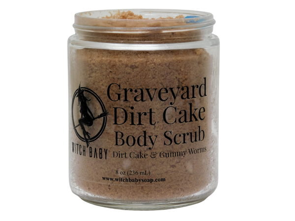 Graveyard Dirt Cake Body Scrub open glass jar showing the cocoa-tinted sea salt scrub with a blue soapy gummy worm embed peeking out of the top, with the Witch Baby label visible