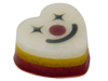 Funhouse Soap angled view showing layered red, yellow, and white heart-shaped bar with clown face on top featuring star eyes, dark red nose, and black smile