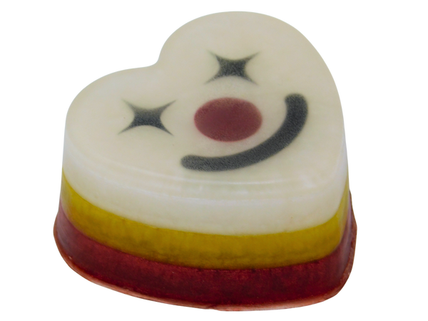 Funhouse Soap angled view showing layered red, yellow, and white heart-shaped bar with clown face on top featuring star eyes, dark red nose, and black smile