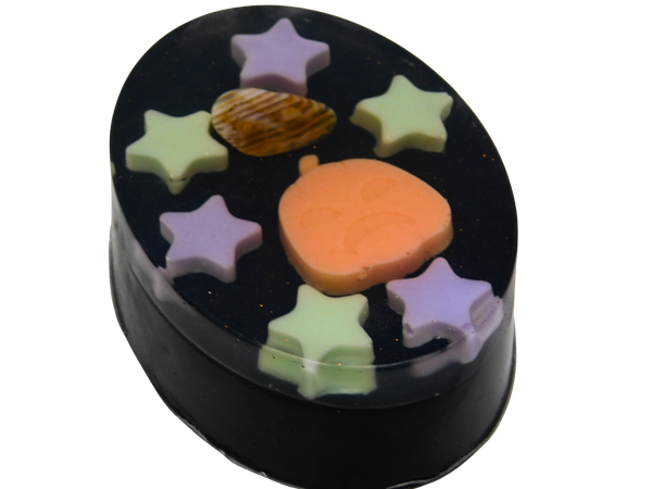 Pumpkin Spell Soap angled view showing the depth of the black oval bar with purple and green star embeds, orange pumpkin, and fire agate crystal on top