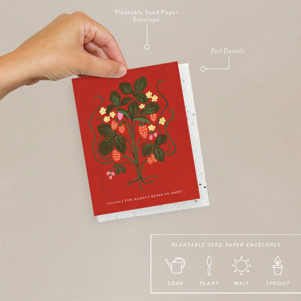 Red card with a strawberry design held by a hand against a beige background