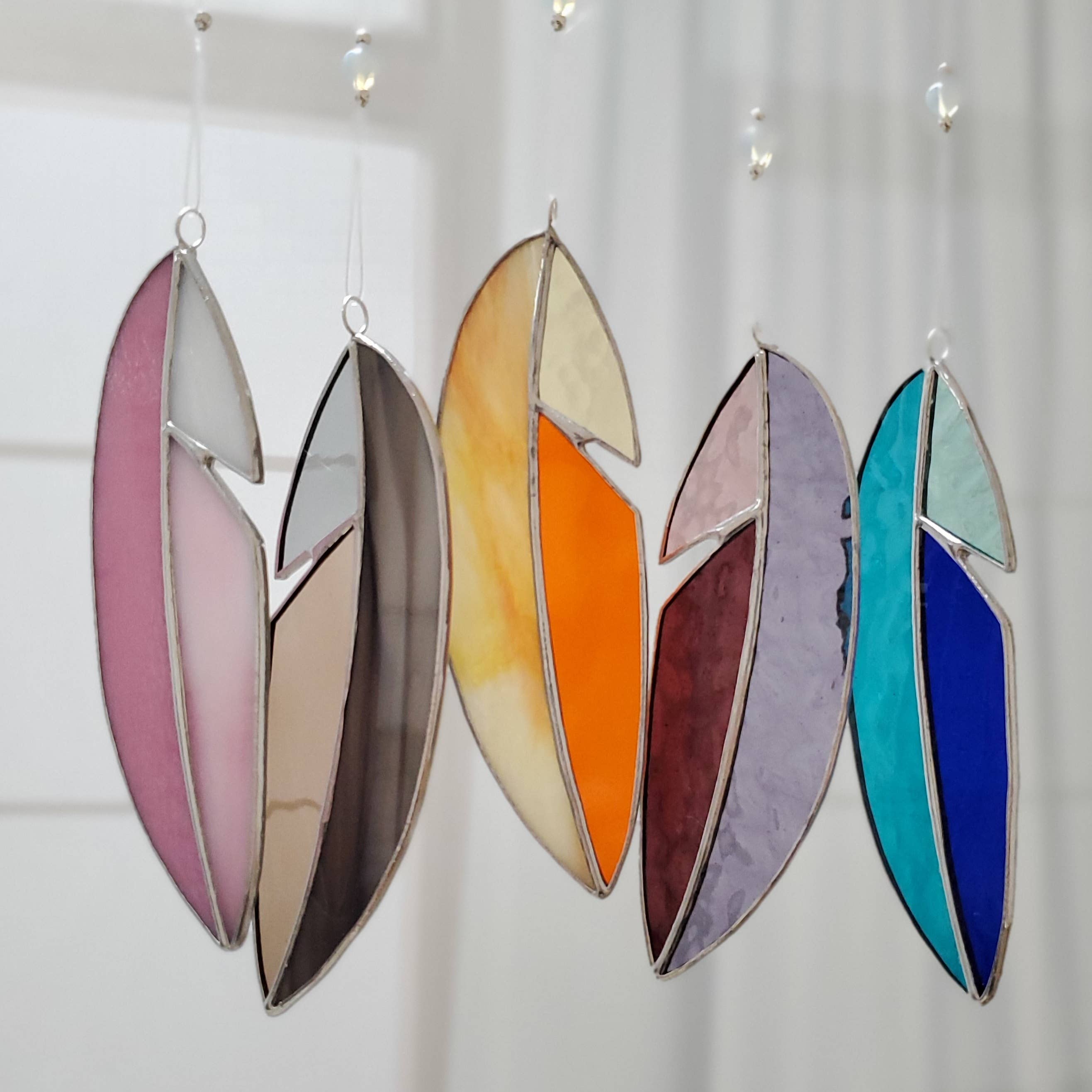Set of colorful glass feather suncatchers hanging against a white background