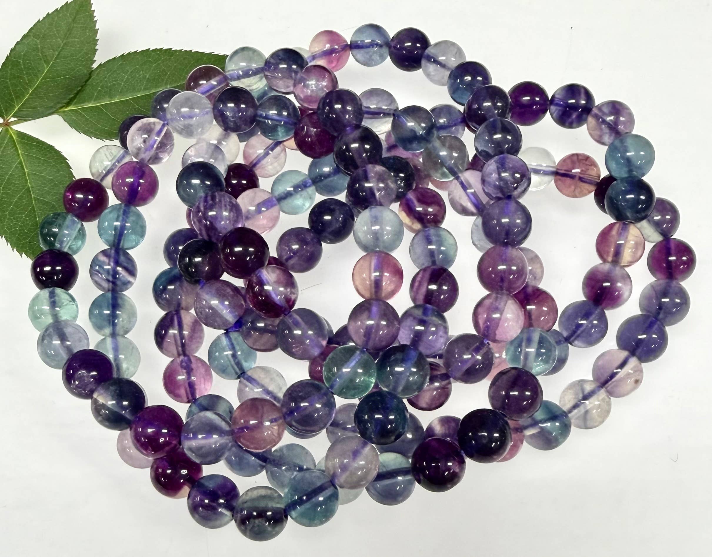 Multicolored beaded bracelets on a white background with a green leaf