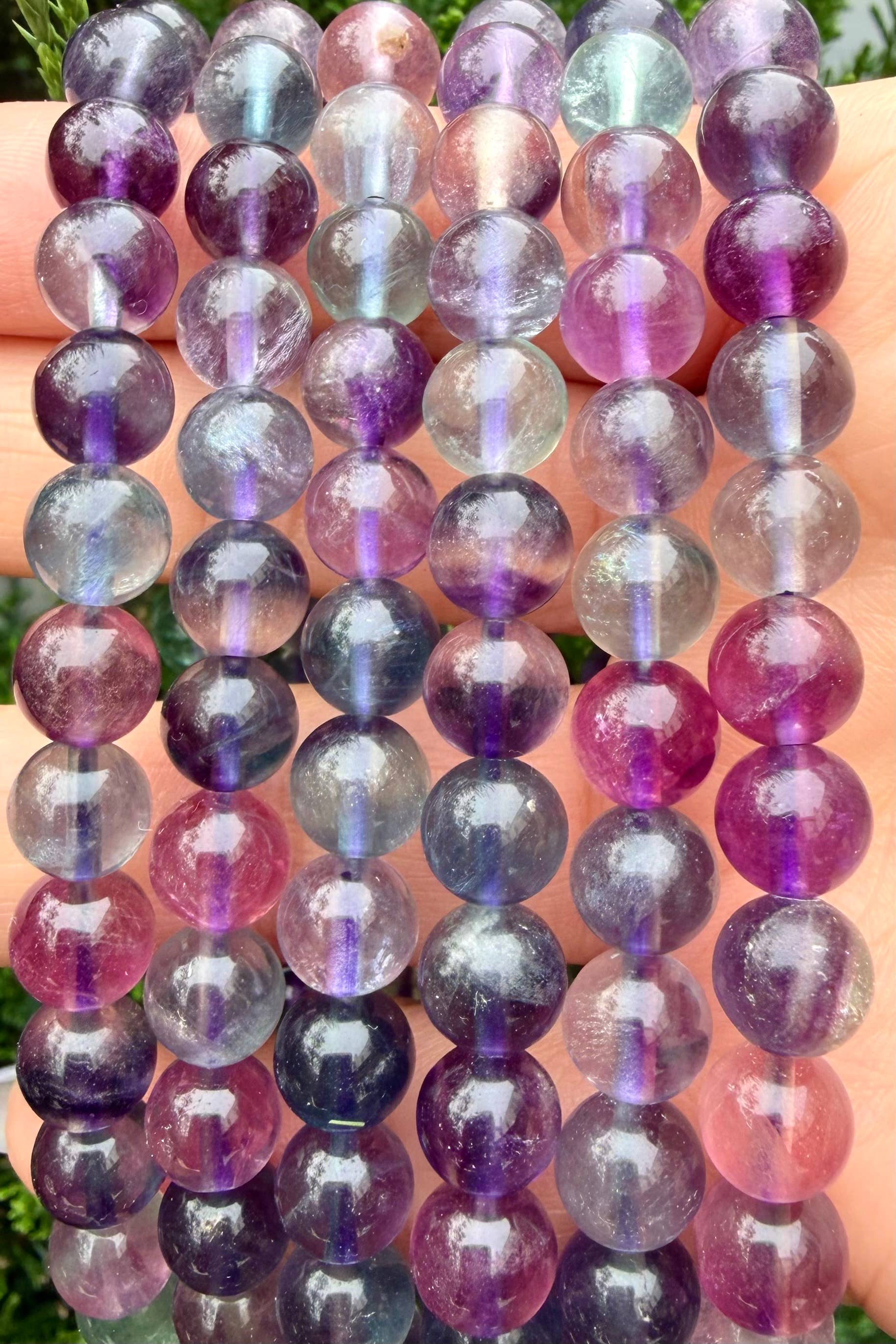 Multicolored gemstone bracelets stacked up on a hand with a blurred natural background