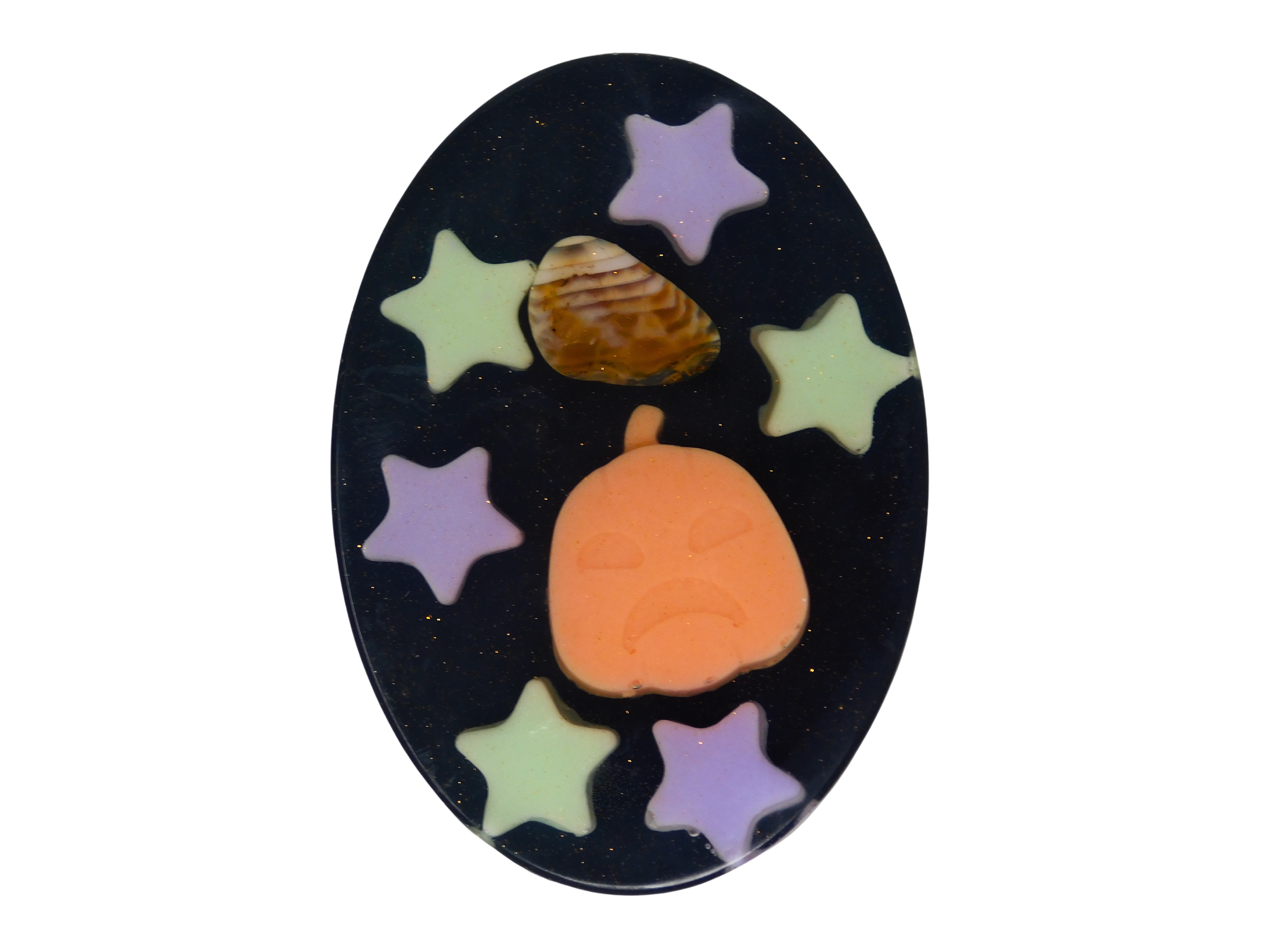 Pumpkin Spell Soap top-down view - black oval soap with purple and green glow star embeds, an orange pumpkin soap embed, and a tumbled fire agate crystal on a white background