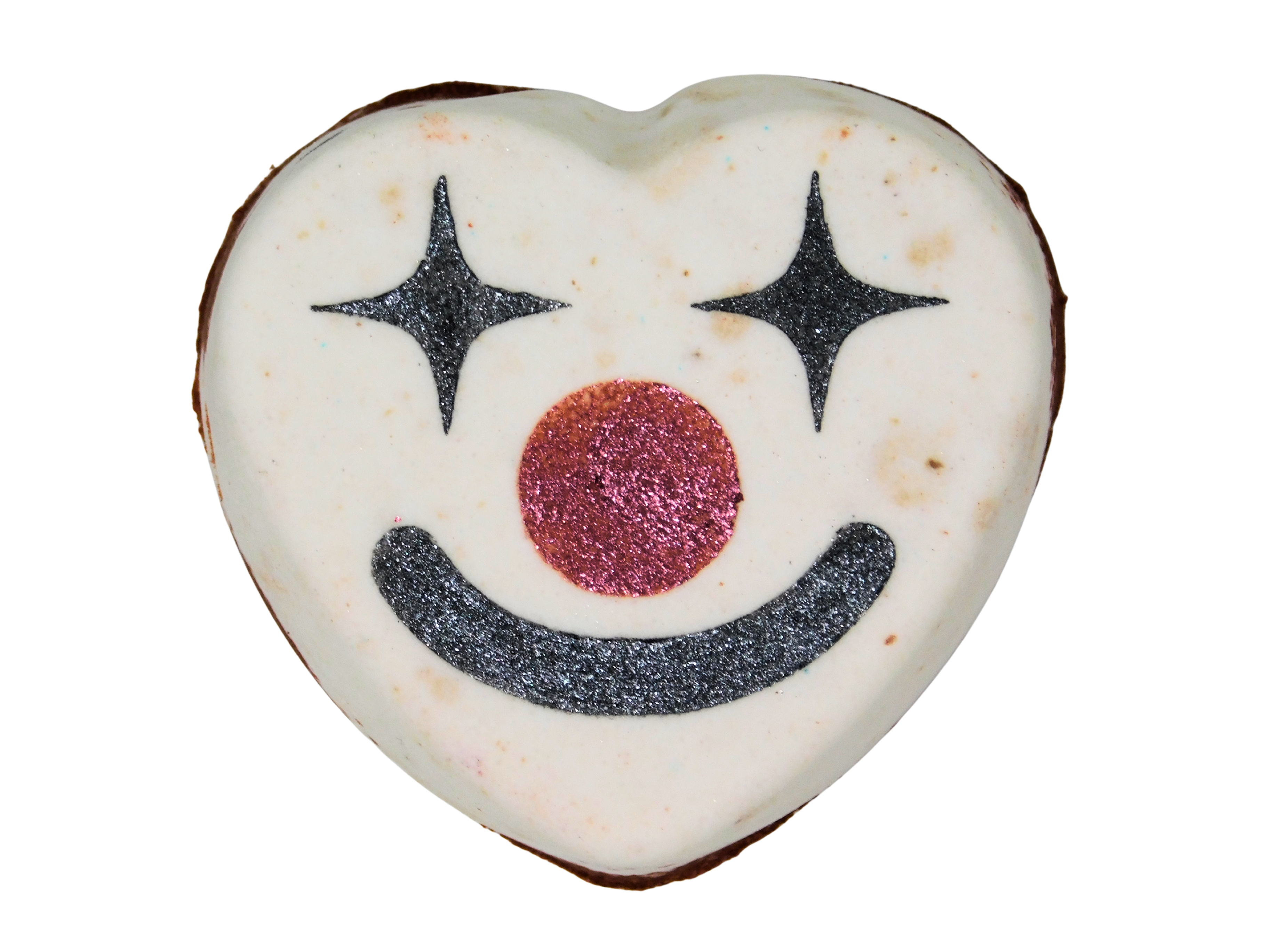 Funhouse Bath Fizz top-down view - white heart-shaped bath fizz with a clown face painted in black glitter star eyes, pink glitter nose, and a black smile, on a white background