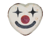 Funhouse Bath Fizz top-down view - white heart-shaped bath fizz with a clown face painted in black glitter star eyes, pink glitter nose, and a black smile, on a white background