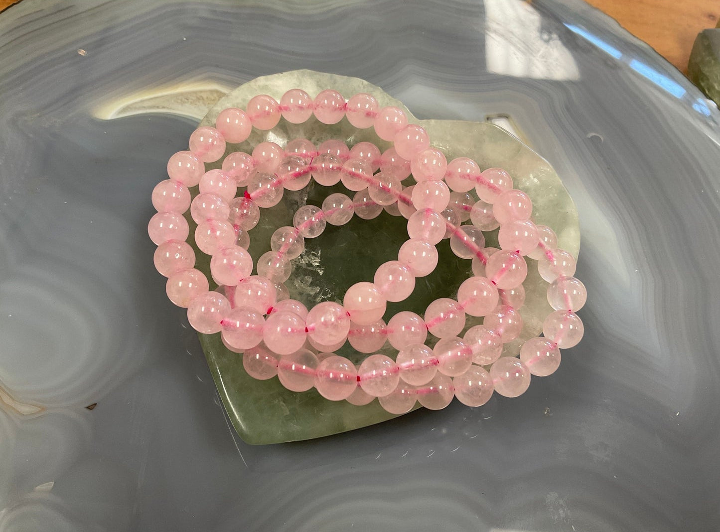 Rose Quartz stretch bracelets sitting on a green crystal heart