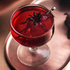Ruby Moon Hibiscus Elderberry Tea brewed as a deep crimson cocktail in a coupe glass garnished with a dried hibiscus flower on a silver tray