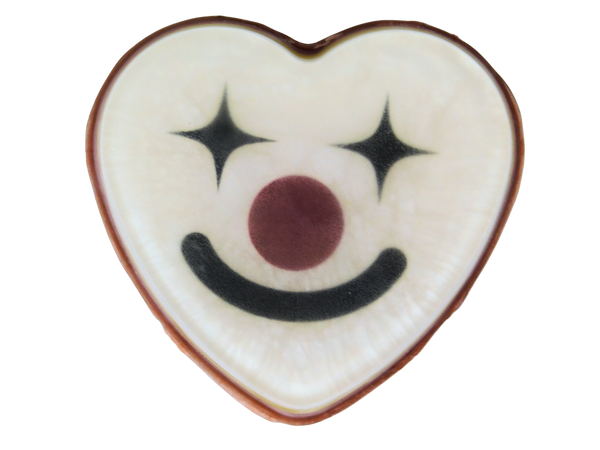 Funhouse Soap top-down view - white heart-shaped soap with a clown face design featuring black four-pointed star eyes, a dark red nose, and a black smile, with a red edge, on a white background