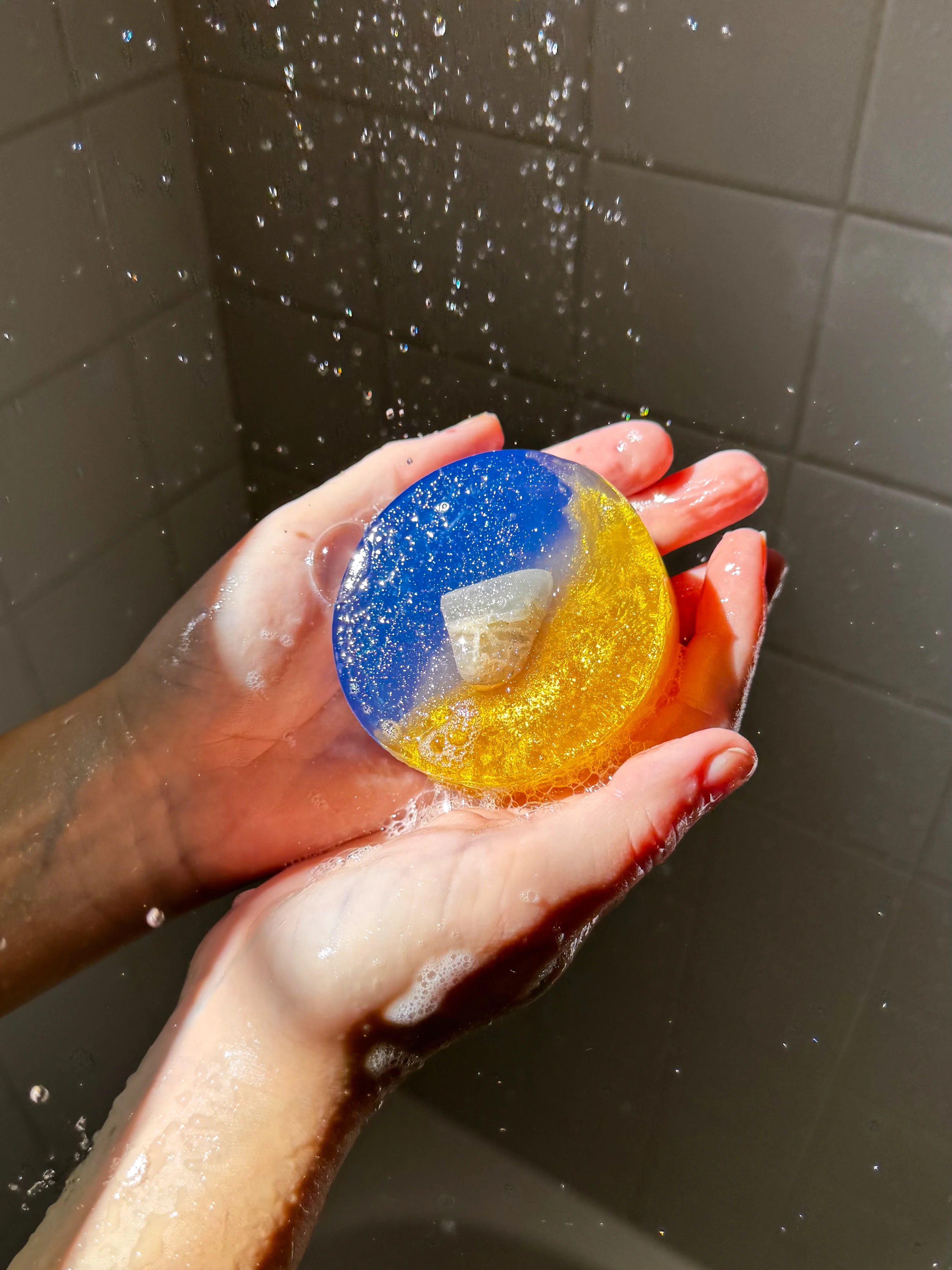 Hand holding a colorful bath soap in a shower setting