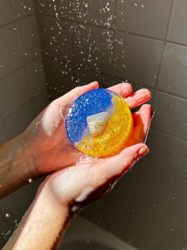 Hand holding a colorful bath soap in a shower setting