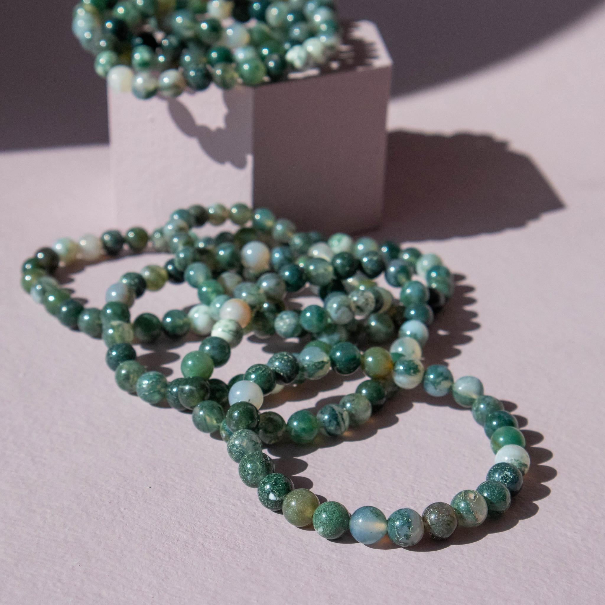 Several green moss agate beaded stretch bracelets on a purple background