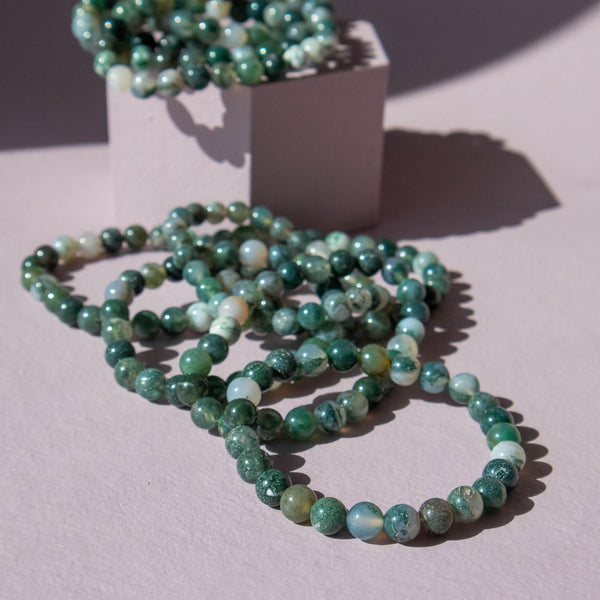 Several green moss agate beaded stretch bracelets on a purple background