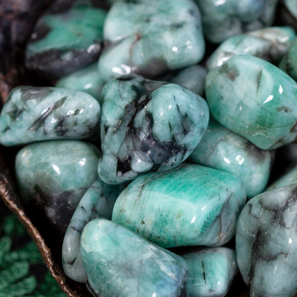 Tumbled emerald stones with greens ranging from brilliant to milky and spots of black
