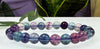 Multicolored beaded bracelet on a white surface with green leaves in the background