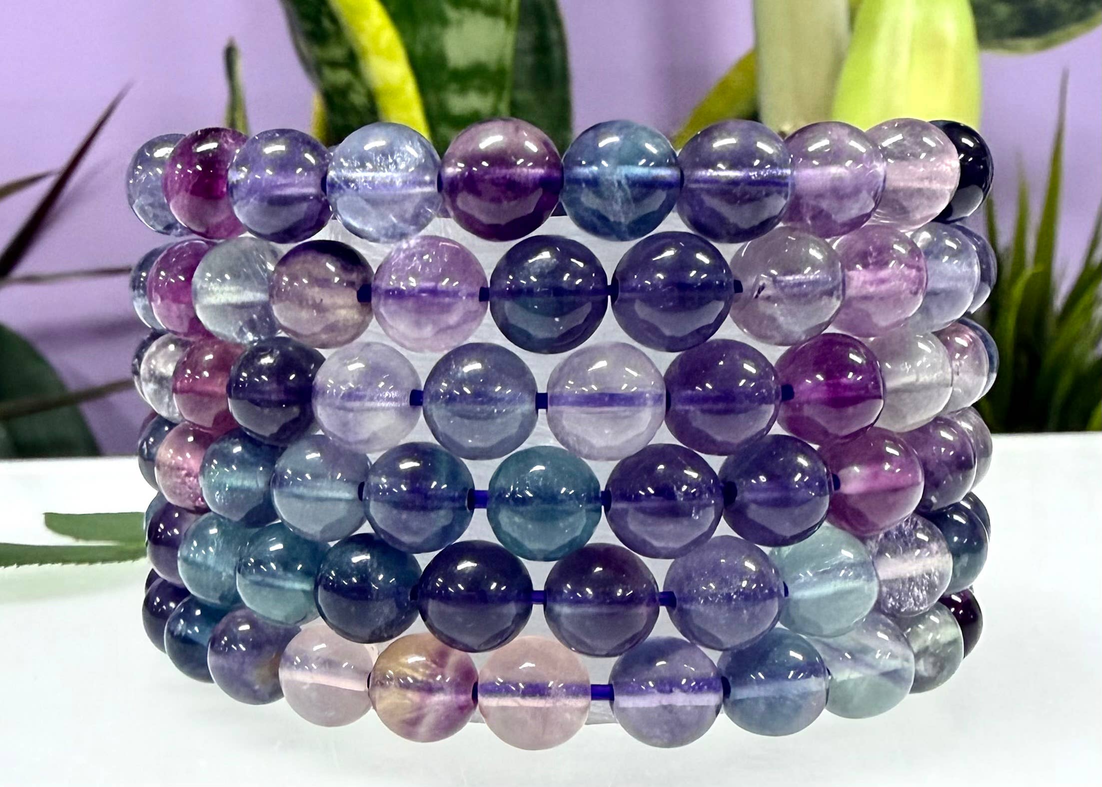 Stack of multicolored beaded bracelets on a white surface with a blurred plant background