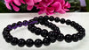 Black beaded bracelet on a white surface with pink flowers in the background