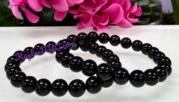 Black beaded bracelet on a white surface with pink flowers in the background