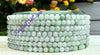 Stack of green beaded bracelets on a white surface with blurred flowers in the background