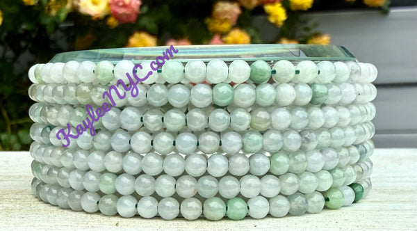 Stack of green beaded bracelets on a white surface with blurred flowers in the background